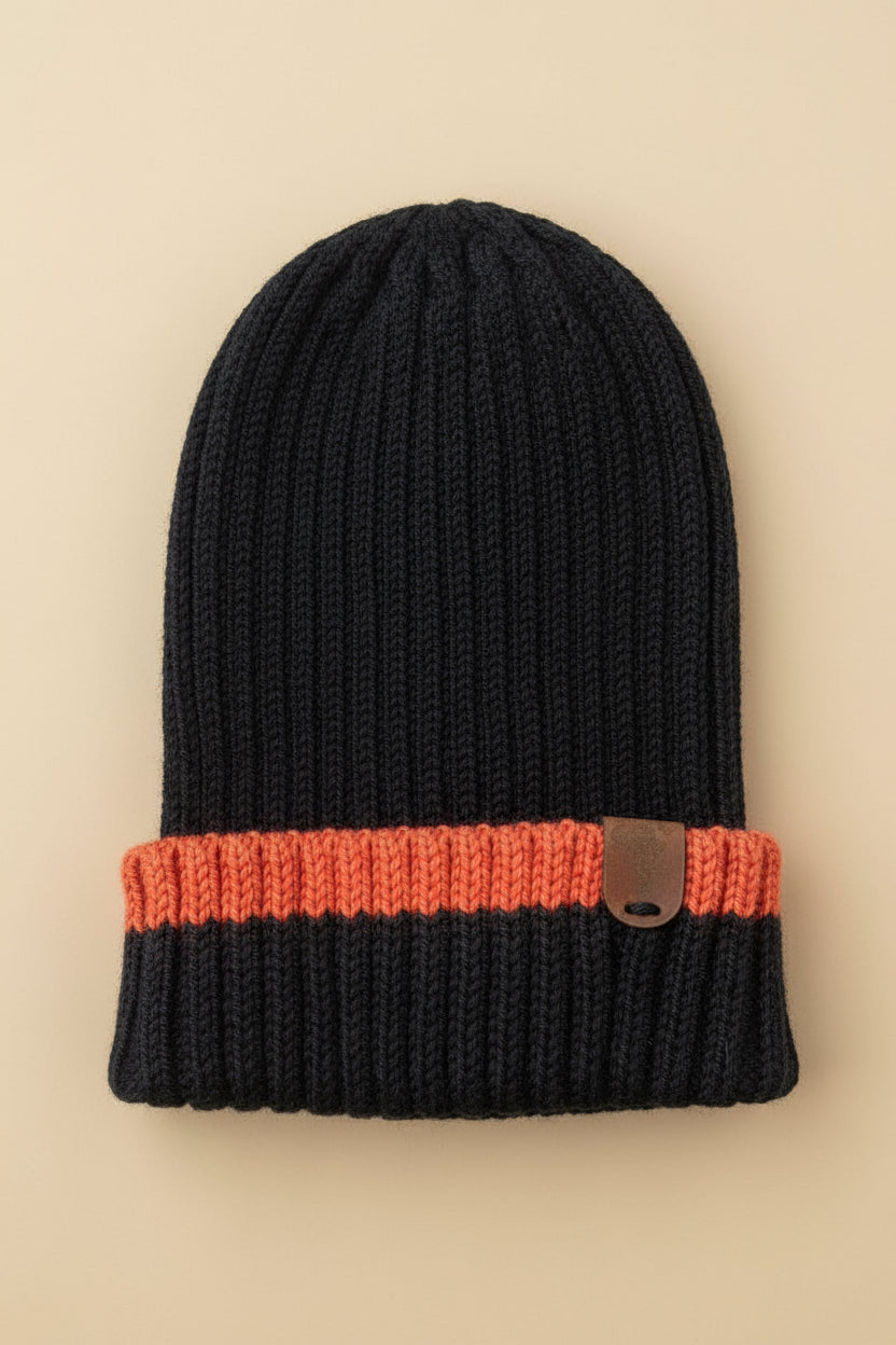 Black merino wool beanie with orange band and brown leather tag on a beige surface