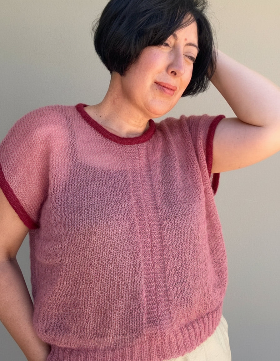 Woman wearing a pink mohair top with cherry trim against a plain background