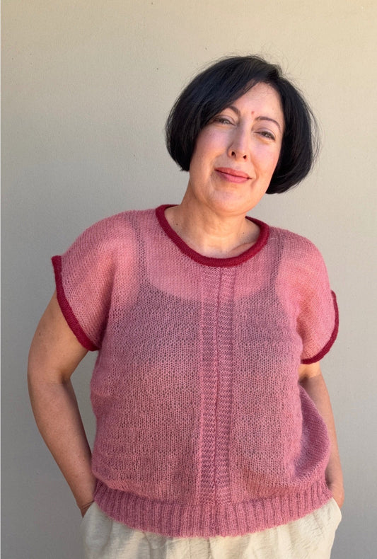 Woman wearing a pink mohair vest with cherry trim against a plain background