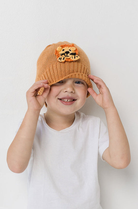 Child wearing a lion-themed orange wool beanie against a white background