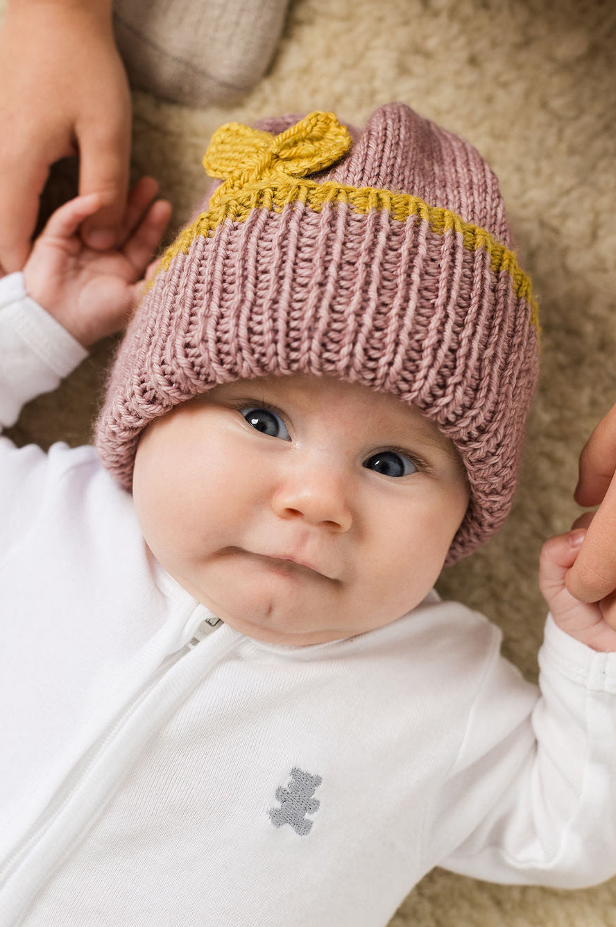 Baby wearing a pink merino wool beanie with a golden butterfly, lying on a sheep skin.