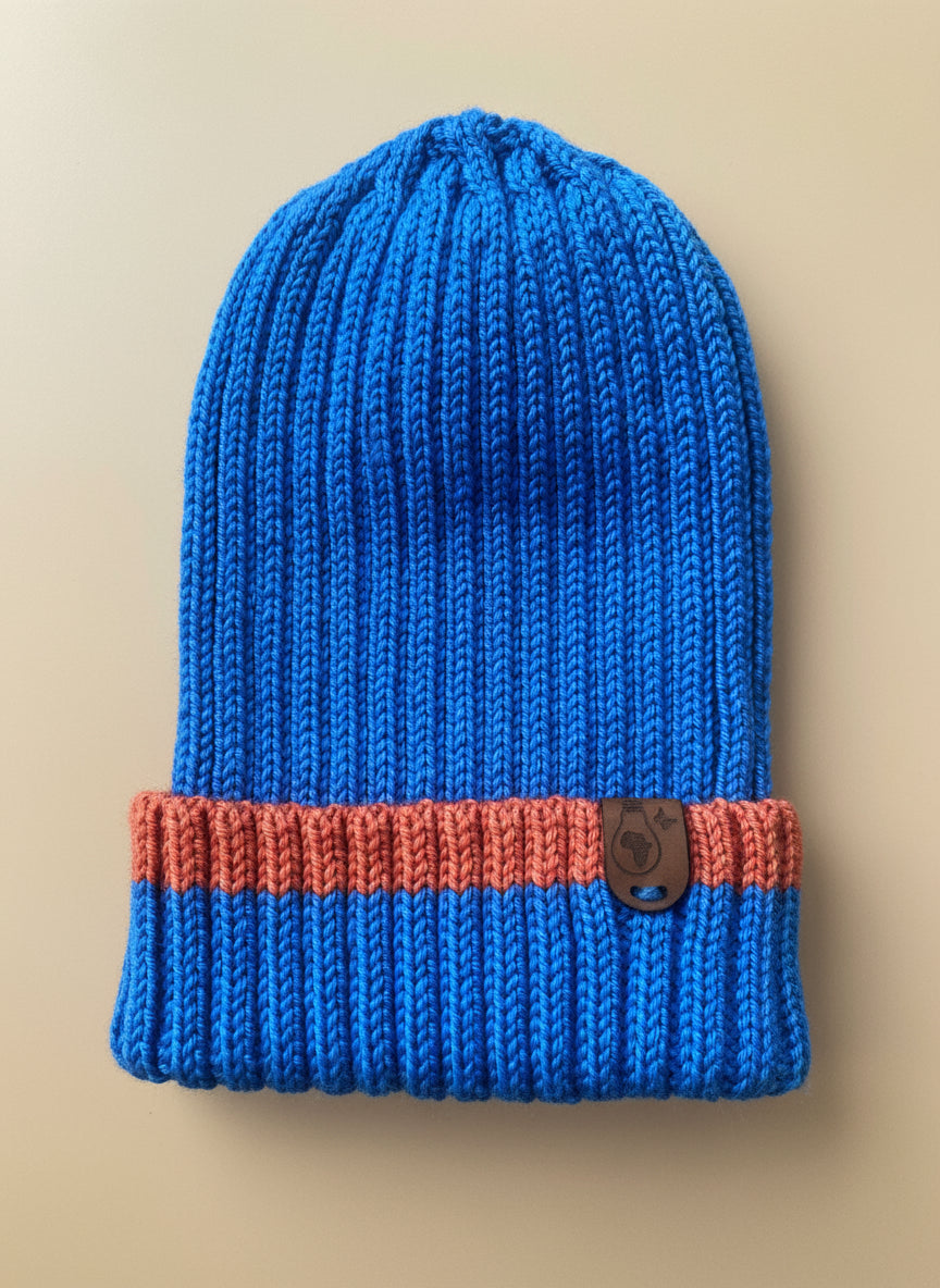 Blue merino wool beanie with an orange stripe on a beige surface