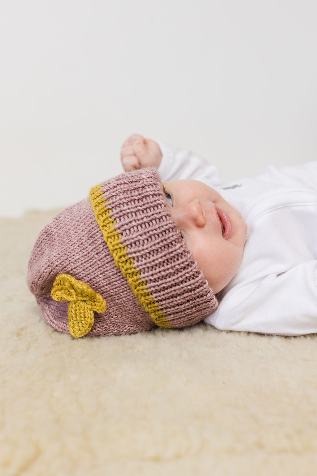Baby wearing a pink and yellow wool beanie on a light background